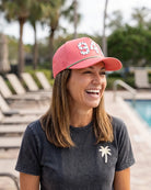 The 941 Signature Hat (Pink) worn on-model by the pool, laughing, three-quarter view: white 941 on a pink crown, perforated panel, green rope.