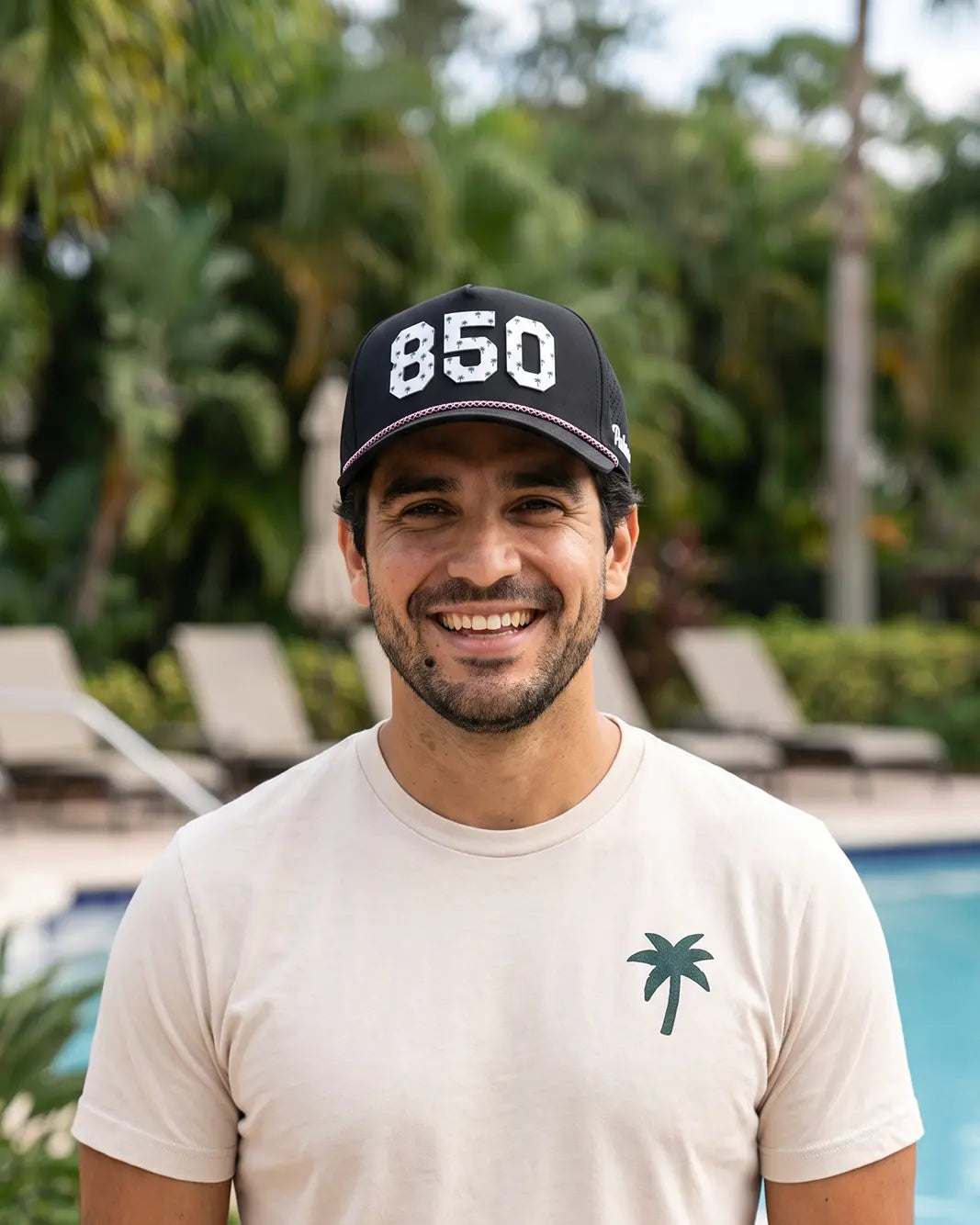 The 850 Signature Hat (Black) worn on-model by the pool, straight-on view: white raised 850 on a black crown with pink and white rope.