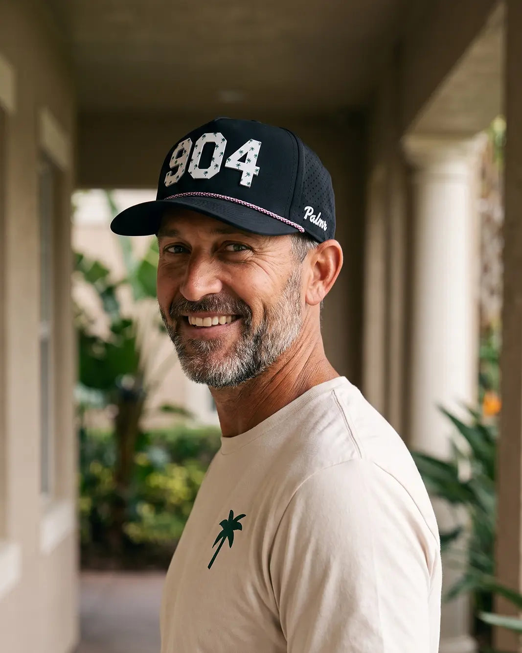 The 904 Signature Hat (Black) worn on-model in a courtyard, looking back over the shoulder: white 904 on a black crown with pink rope and Palmr script.