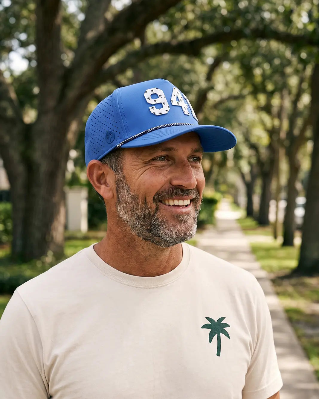 The 941 Signature Hat (Blue) worn on-model on an oak-lined path, three-quarter view: white 941 on a blue crown, perforated panel, black and white rope.