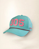 A turquoise baseball cap with pink star-patterned '305' lettering on the front and a thin red-and-white dotted stripe across the brim, shown against a plain light beige background.