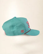 A teal perforated baseball cap with a pink embroidered number 3 on the side and a small pink circular logo patch, shown against a plain cream background.