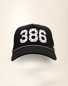 The 386 Signature Hat (Black), front view: white raised 386 with small palm print on a black crown, pink and white rope along the brim.