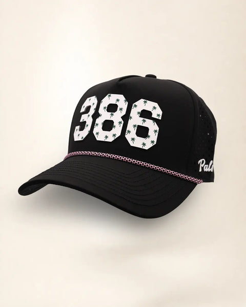 The 386 Signature Hat (Black), three-quarter view: white raised 386 with small palm print on a black rope snapback, pink and white rope, white Palmr script.