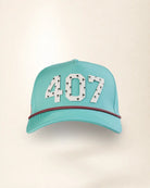 A light turquoise baseball cap featuring the number '407' in white with black star patterns on the front, and a red and black patterned rope detail across the brim.