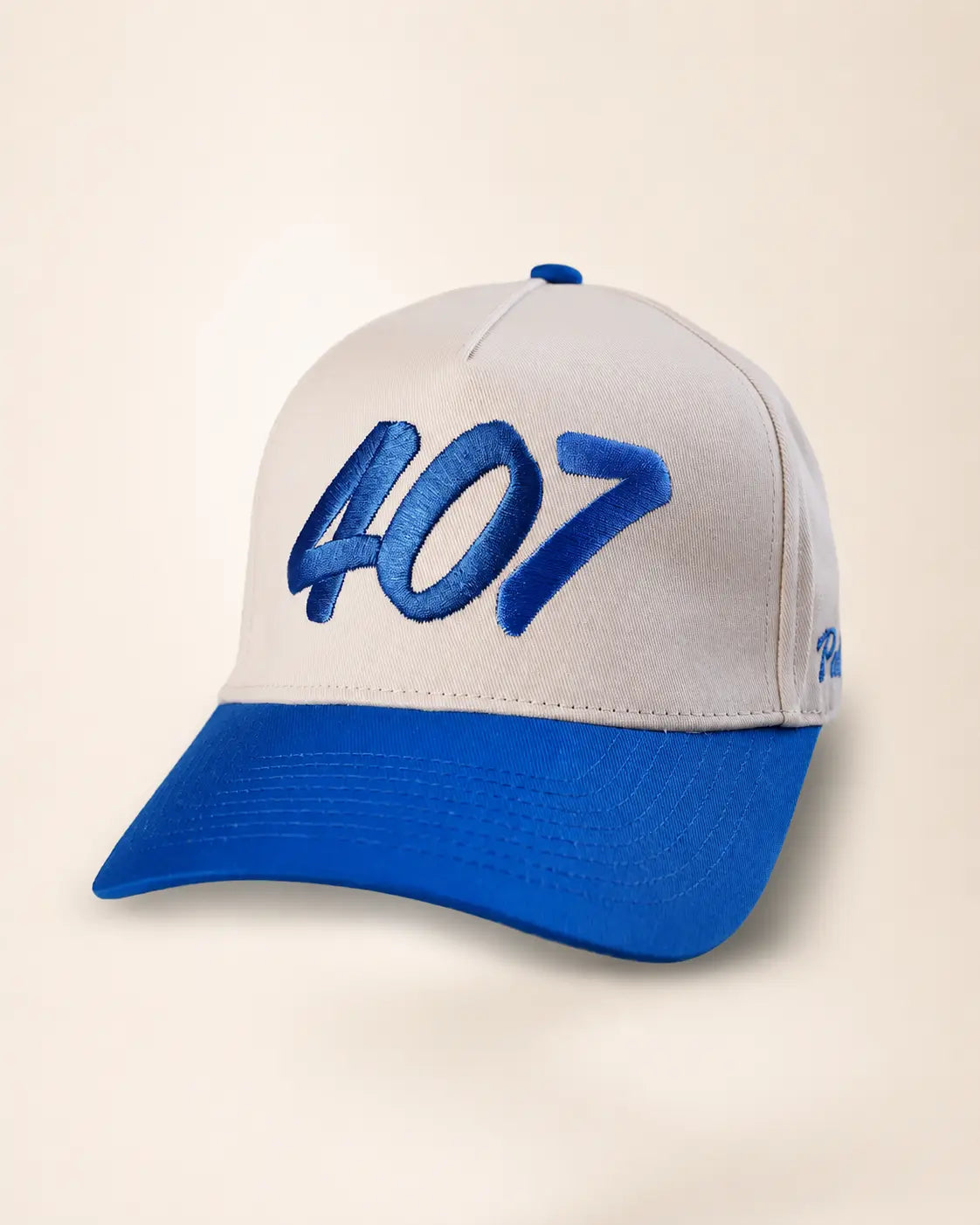 A two-tone baseball cap with a white crown and a royal blue brim, featuring large blue embroidered '407' text on the front and a small blue embroidered logo on the side, set against a plain beige background.