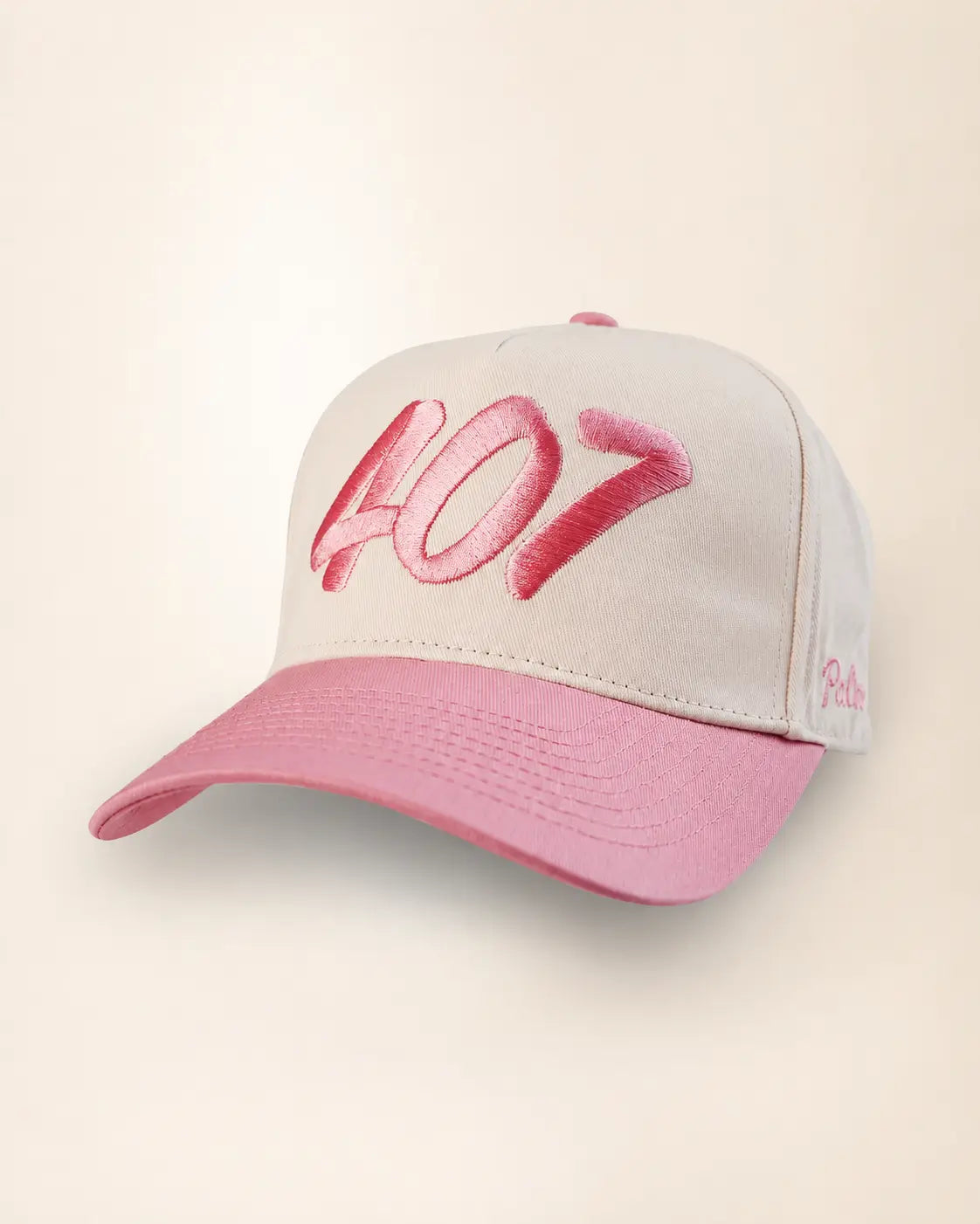 A baseball cap with a light gray crown and a pink brim, featuring a large pink embroidered '407' on the front and a small pink script logo on the side, set against a plain cream background.