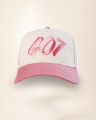 A baseball cap with a white crown, pink brim, and pink embroidered '407' text on the front, shown against a light beige background.