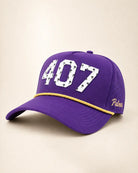 A purple baseball cap with '407' in white varsity-style lettering on the front, a thin gold chain detail across the brim, and 'Palmr' embroidered in gold on the side, set against a light beige background.