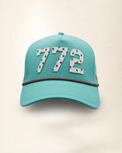 The 772 Signature Hat (Teal), front view: white raised 772 with small palm print on a teal crown, pink and black rope along the brim.