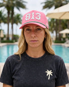 A woman wearing the pink 813 Signature Hat and a charcoal palm tree tee, standing by a pool.