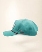 The 904 Signature Hat (Teal), left side view: pink Palmr script, perforated side panel, pink and black rope on the brim, edge of the white 904.