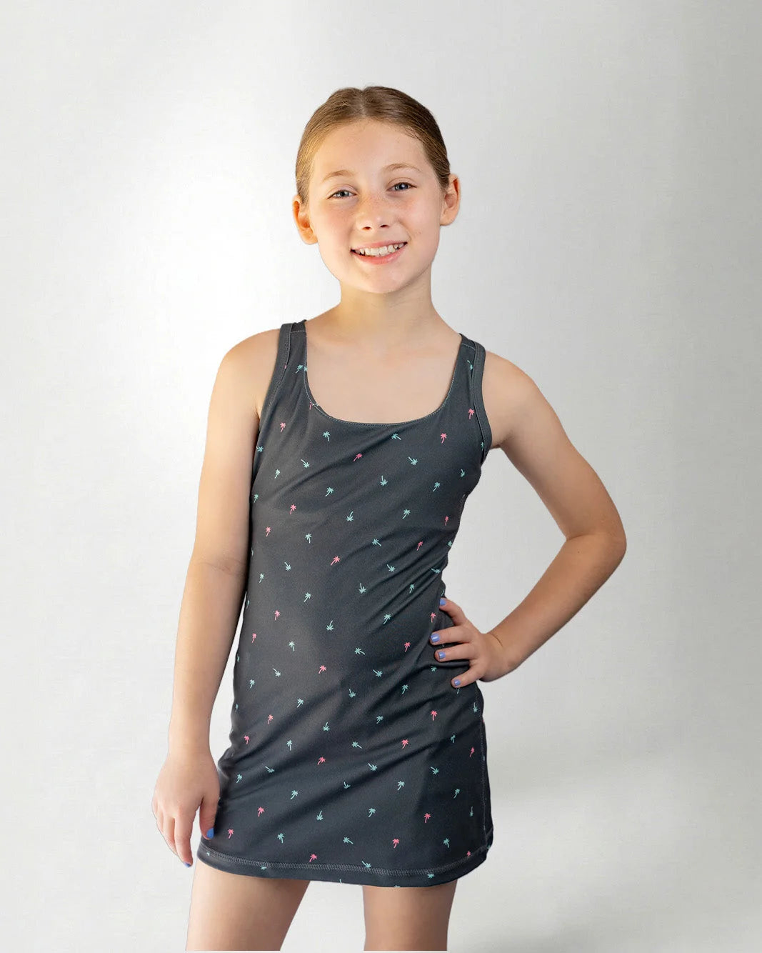 Young girl wearing a dark gray tank dress with small patterns on a white background