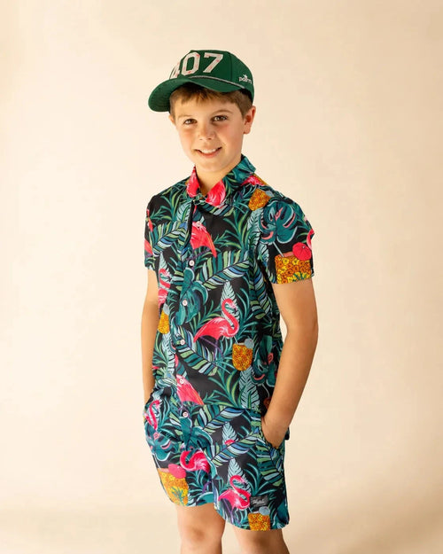 Boy wearing Baha Palm Kids Button Up with tropical print of monstera leaves, palm fronds, flamingos, and pineapples