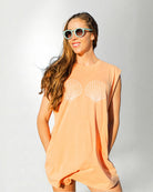 Woman wearing a peach-colored sleeveless top with shell designs on a white background