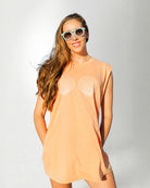 Woman wearing a peach-colored sleeveless top with shell designs on a white background