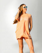 Woman wearing a peach-colored sleeveless top with shell designs on a white background