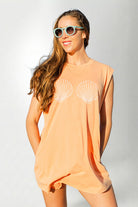 Woman wearing a peach-colored sleeveless top with shell designs on a white background