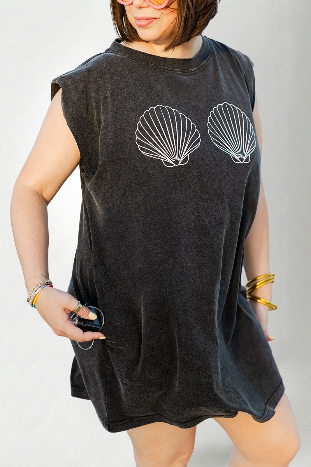 Person wearing a black sleeveless dress with shell designs on a plain background