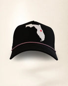 A black baseball cap featuring a white silhouette patch of the state of Florida on the front with a small red dot marking, and a thin metallic rose gold chain trim across the brim.