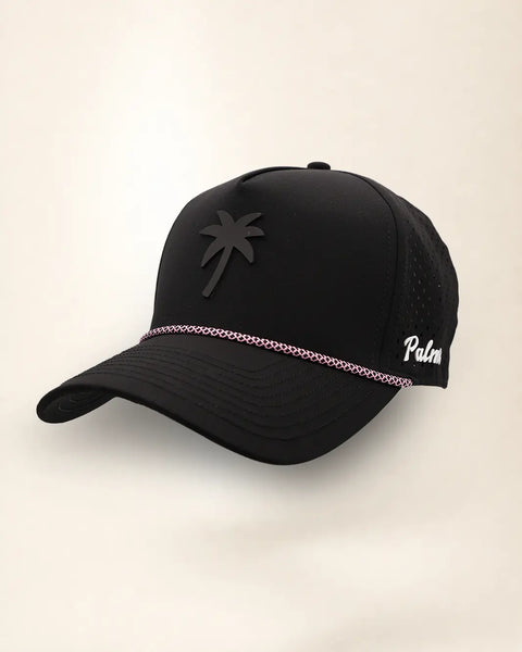 The Palm Icon Signature Hat (Midnight), three-quarter view: black tonal palm tree icon on a black rope snapback, pink and white rope, white Palmr script.