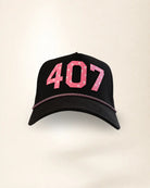 A black baseball cap featuring the number '407' in pink with white palm patterns on the front, and a thin pink chain detail along the edge of the brim, set against a plain off-white background.