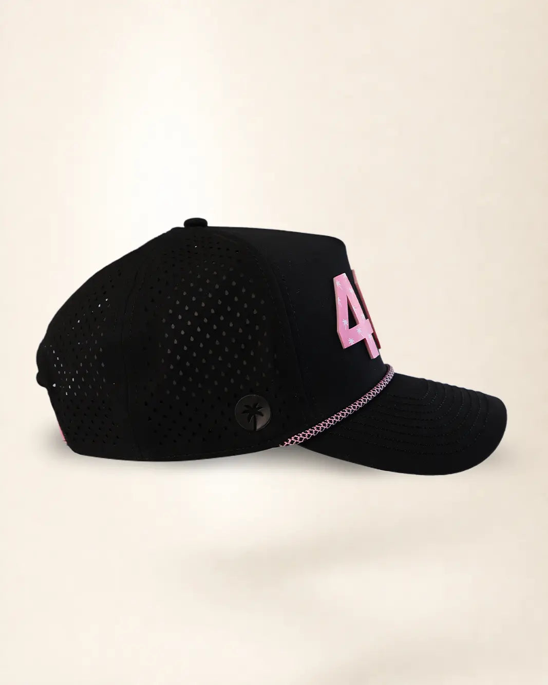 A black mesh baseball cap with a pink embroidered number 4 on the side and a pink-and-white patterned trim along the edge of the brim, shown against a plain light beige background.