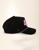 A black mesh baseball cap with a pink embroidered number 4 on the side and a pink-and-white patterned trim along the edge of the brim, shown against a plain light beige background.