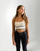 Woman wearing a white and black strapless top with black leggings on a plain background