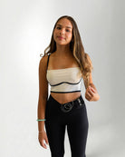 Woman wearing a white and black strapless top with black leggings on a plain background