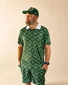 The Club Palm Polo in palm green with geometric diamond pattern and palm tree details, styled poolside on a sunny day