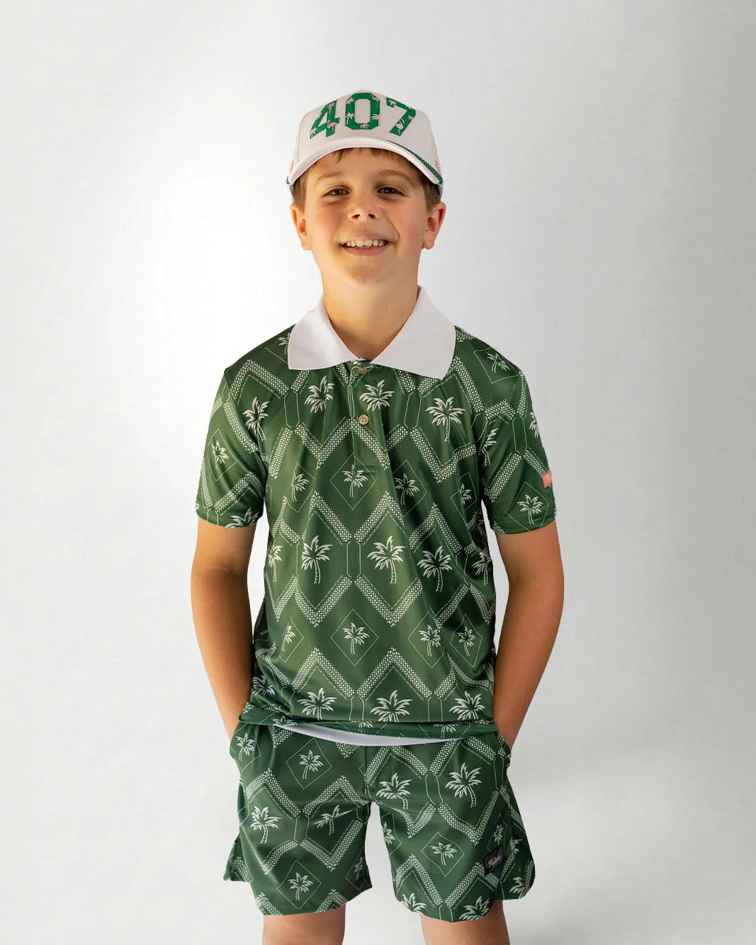 Child wearing a green patterned outfit with a cap on a white background