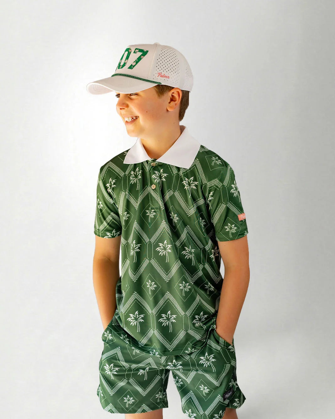 Child wearing a green patterned outfit with a cap on a white background
