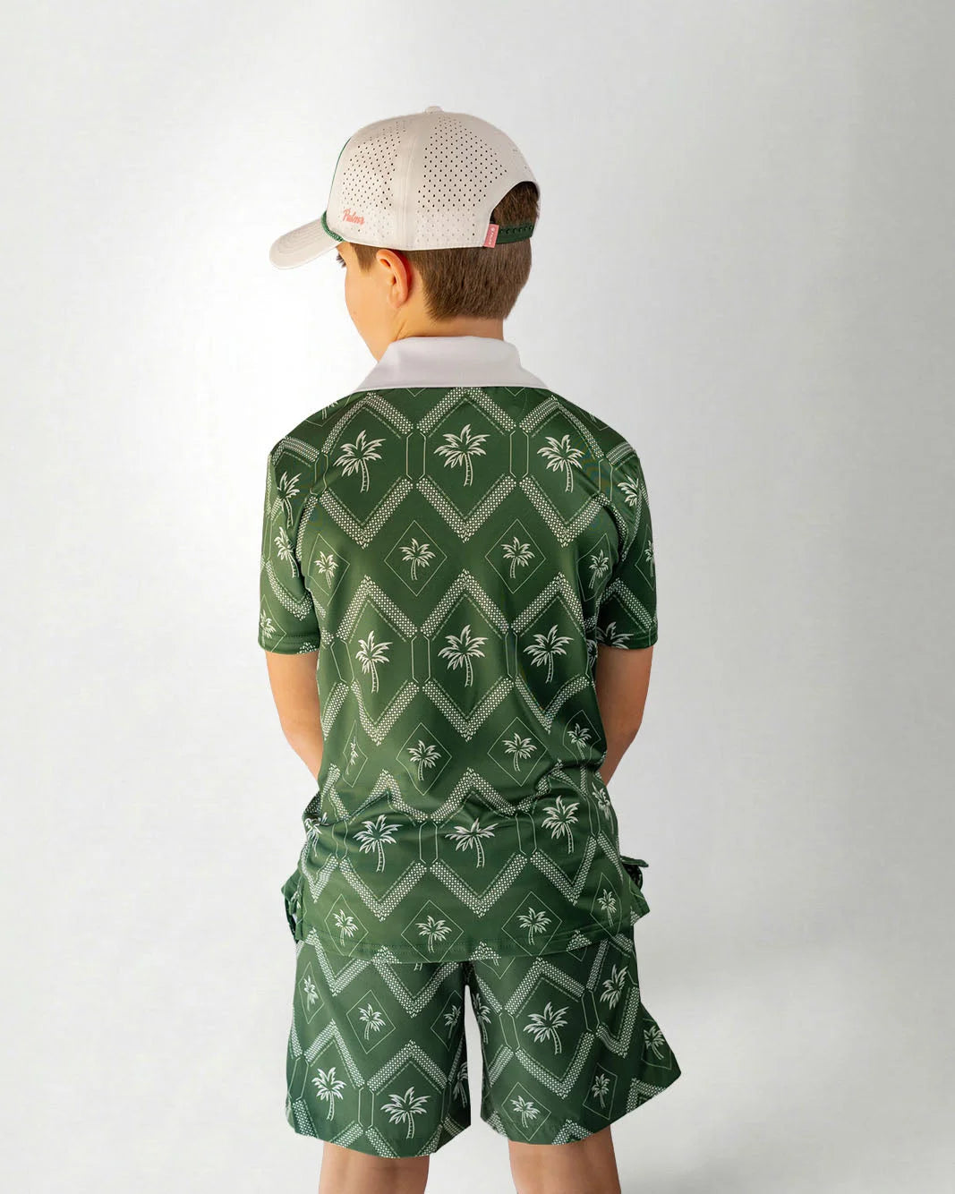 Person wearing a green patterned outfit with a cap on a white background