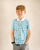 The Palmr Coastal Bay Kids Polo in teal with white collar, featuring palm tree and flamingo icons, moisture-wicking and quick-dry fabric for active kids