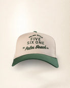 A structured trucker-style baseball cap with a cream-colored front panel and a dark green curved brim. The front panel features embroidered text reading 'PALMR STYLE FIVE SIX ONE 20 Palm Beach 25' in dark green.