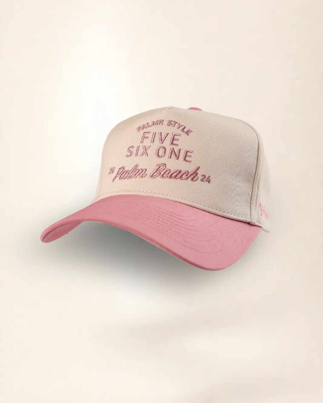 A two-tone baseball cap with a light beige front panel and a dusty pink brim, featuring embroidered text on the front.