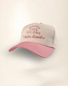 A two-tone baseball cap with a light beige front panel and a dusty pink brim, featuring embroidered text on the front.