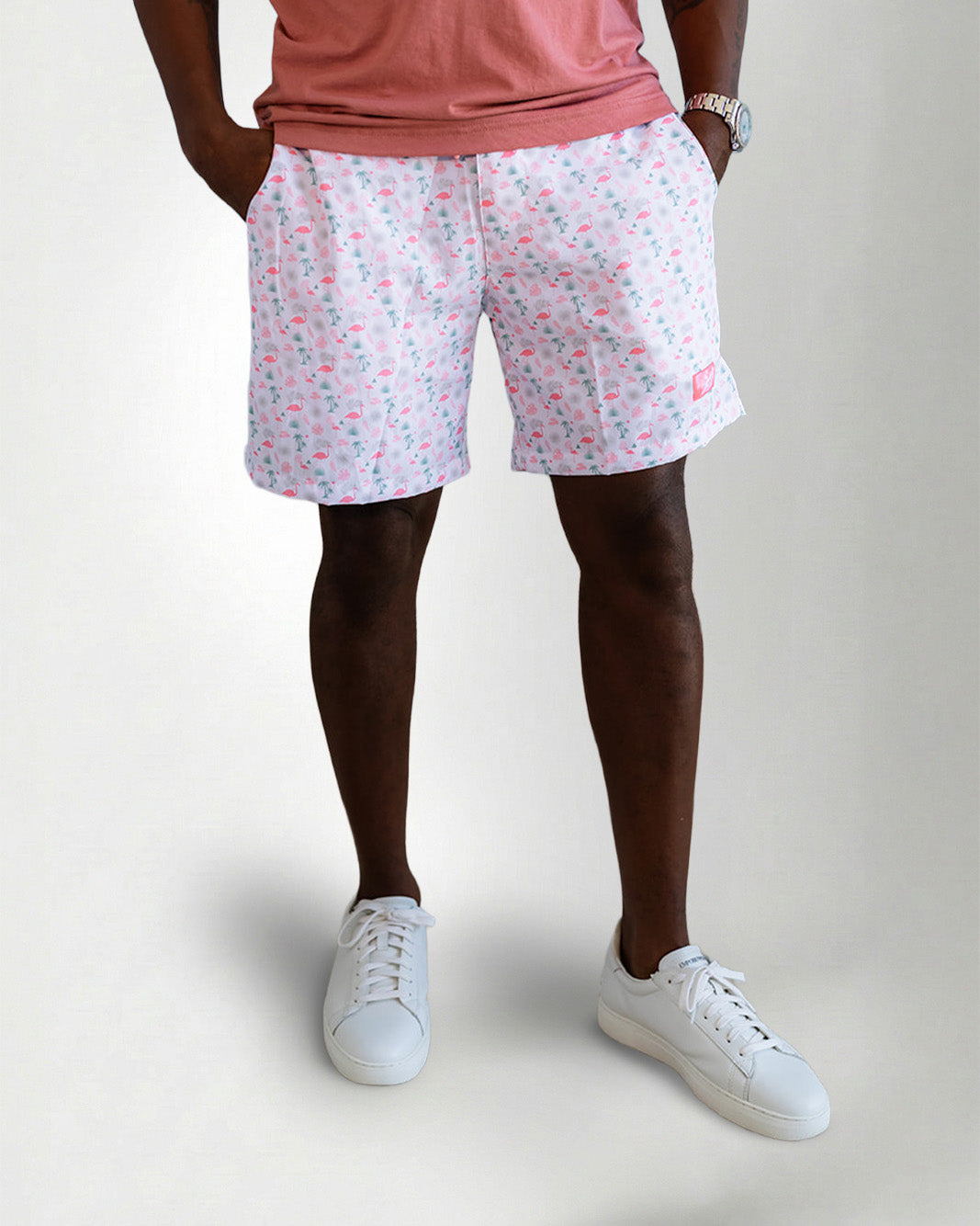 Person wearing pink flamingo shorts and white sneakers on a plain background