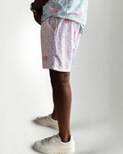 Person wearing pink floral shorts and white sneakers on a plain background