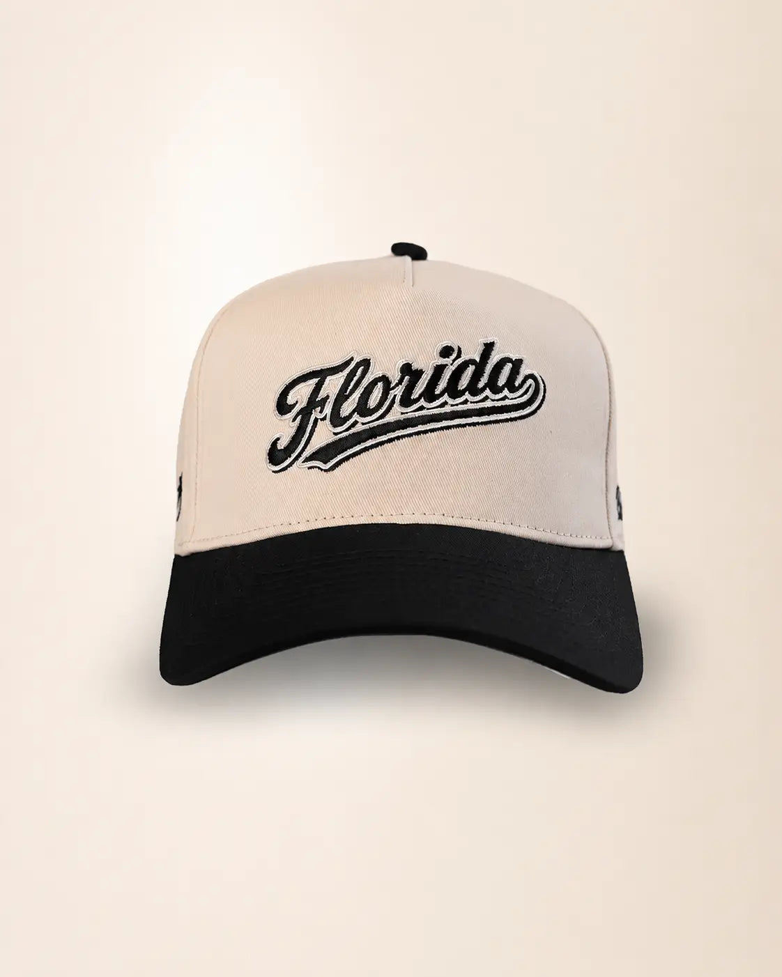 A two-tone baseball cap with an off-white crown and a black curved brim, featuring the word 'Florida' embroidered in black script across the front.
