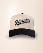 A two-tone baseball cap with an off-white crown and a black curved brim, featuring the word 'Florida' embroidered in black script across the front.