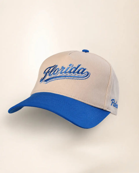 The Florida Heritage Hat (Blue): sand and blue two-tone cap with Florida embroidered in blue script, blue brim, Palmr script on the side.