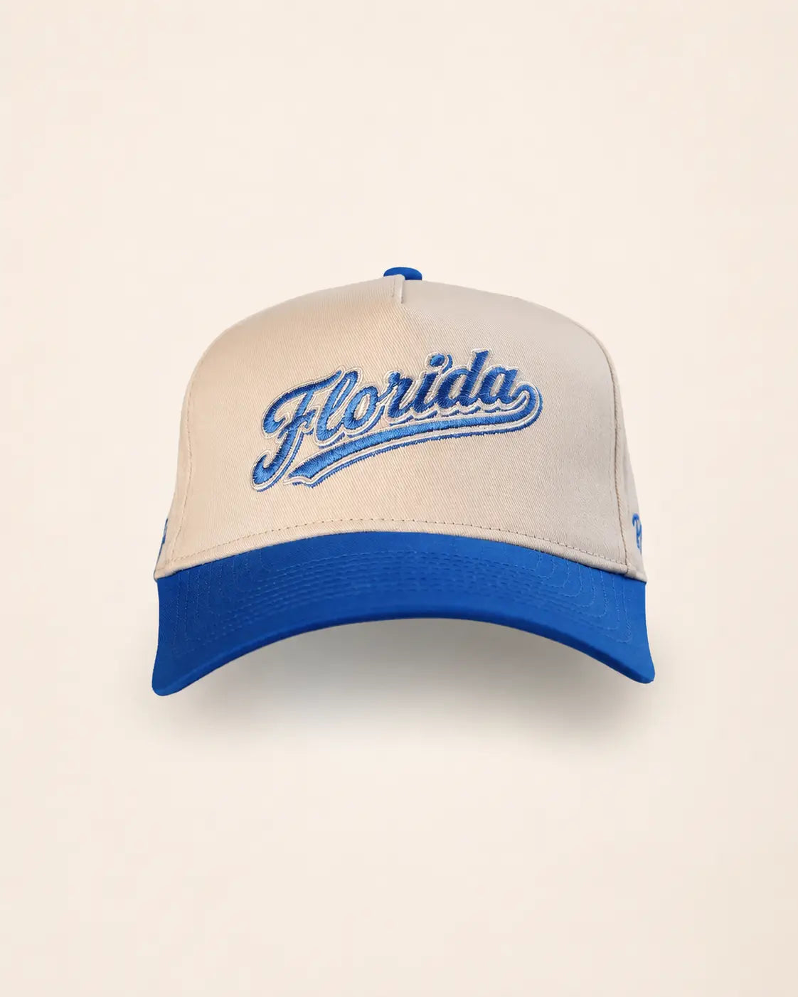 A structured baseball cap with a cream-colored front panel and brim, featuring a royal blue curved brim, blue button on top, and 'Florida' embroidered in blue script across the front.