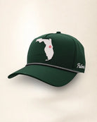 The Florida Signature Hat (Green), three-quarter view: white raised Florida silhouette with a pink dot at Orlando on a dark green rope snapback, braided rope, white Palmr script.