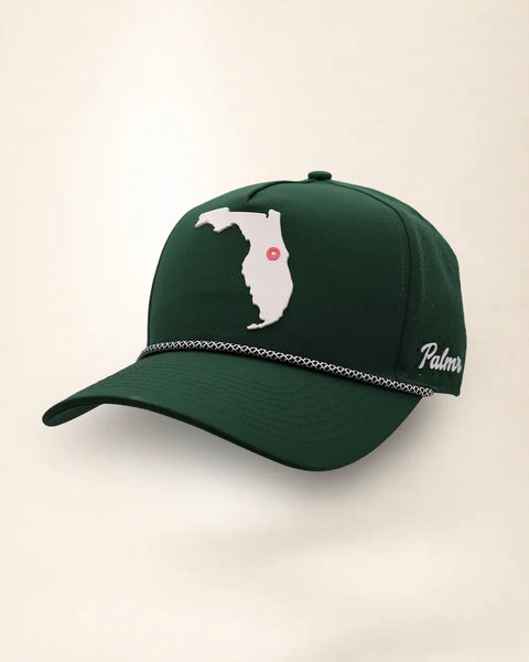 The Florida Signature Hat (Green), three-quarter view: white raised Florida silhouette with a pink dot at Orlando on a dark green rope snapback, braided rope, white Palmr script.