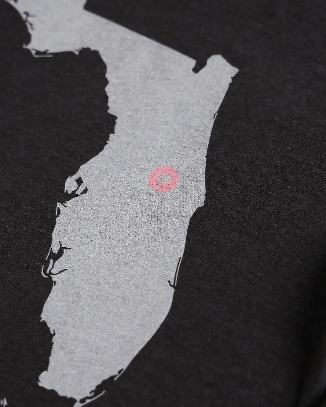 Close-up of a black t-shirt featuring a light gray map graphic of Maine with a small pink circle marking the location of Portland.