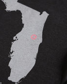 Close-up of a black t-shirt featuring a light gray map graphic of Maine with a small pink circle marking the location of Portland.