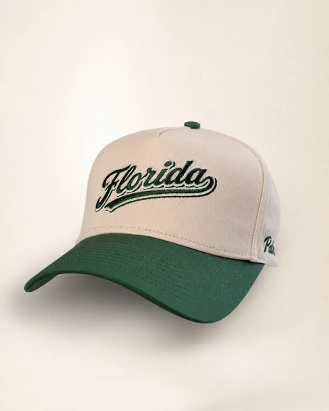 The Florida Heritage Hat (Green): cream and dark green two-tone, Florida embroidered in green script on the front, Palmr script on the side.