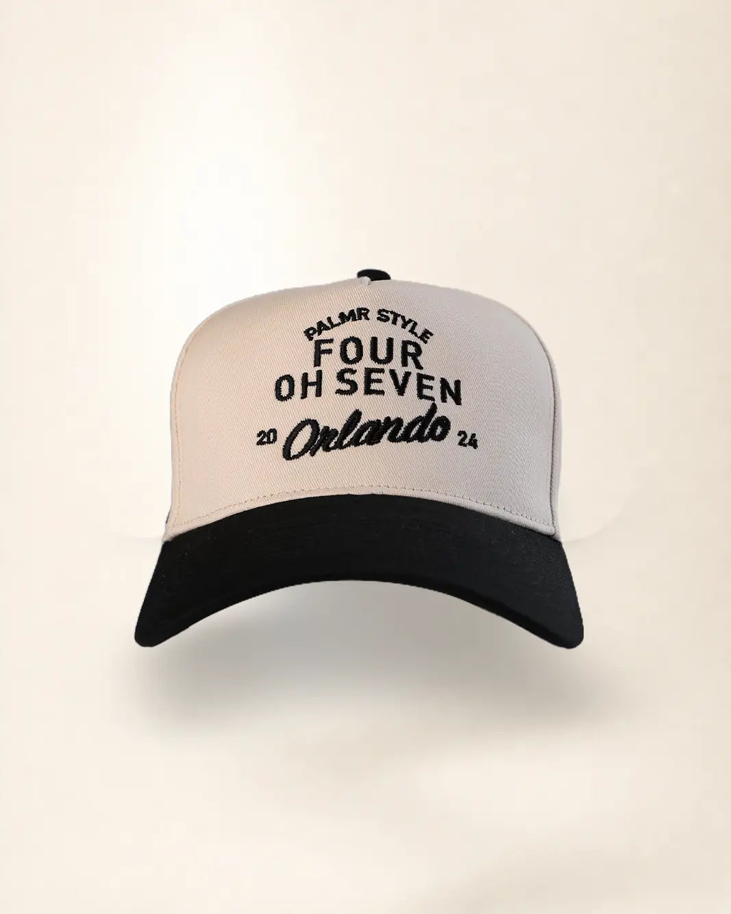 A two-tone baseball cap with a white front panel and black brim, featuring black embroidered text that reads 'PALMR STYLE FOUR OH SEVEN 2024 Orlando' on a clean, light beige background.